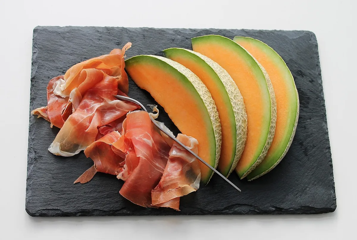 mains gantées coupant une tige de melon au-dessus d'une feuille