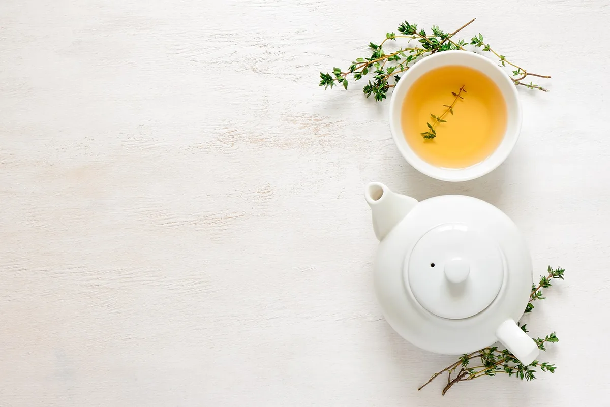 Tasse de tisane avec herbes séchées à côté d'une bouilloire