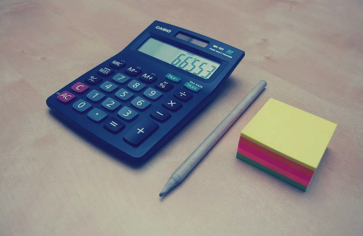 Table de travail avec plans immobiliers, calculatrice et notes, mains anonymes